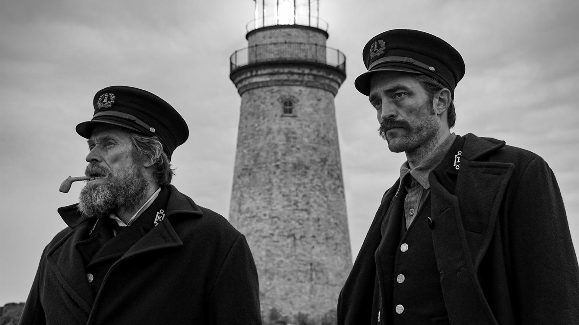 Willem Dafoe e Robert Pattinson em frente a um farol isolado na costa do Maine em O Farol (2019)