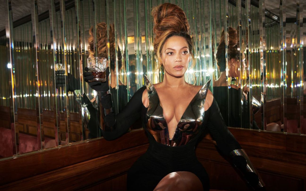 Beyoncé holds a drink next to a mirrored wall